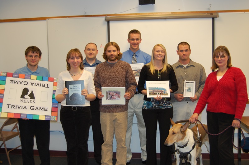 Group of students smiling for the camera holding books with a service dog