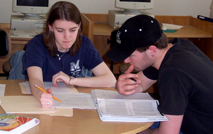 one student tutoring another at a table with notebooks open