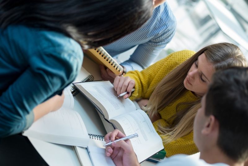 four students looking at books on a table and taking notes