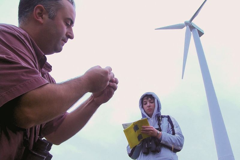 Professor and student working in the field with a wind turbine in the background