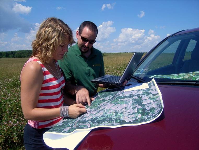 Two people looking at a map on the hood of a car in a rural area