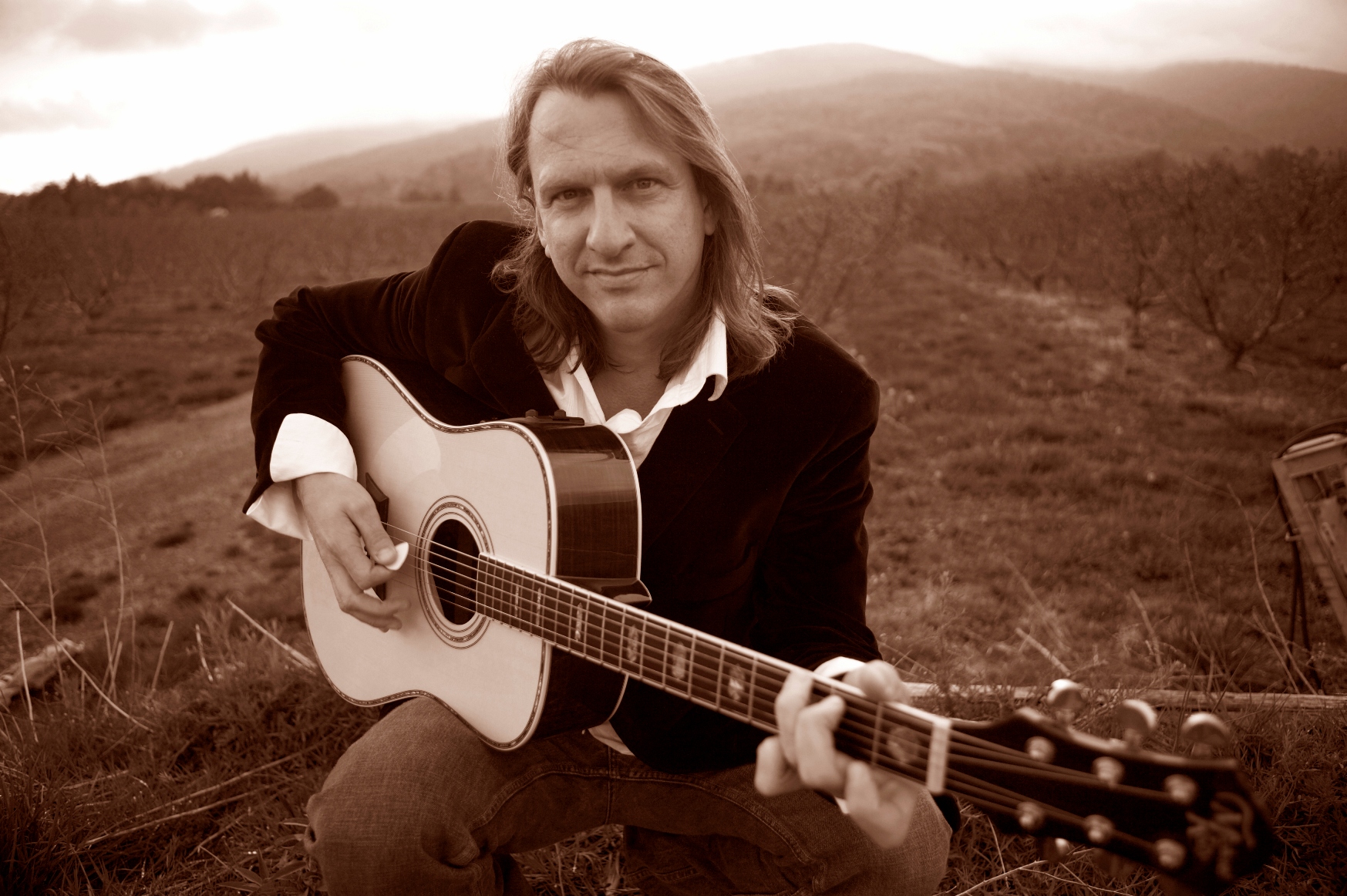 Photo of Ellis Paul holding a guitar in sepia tone