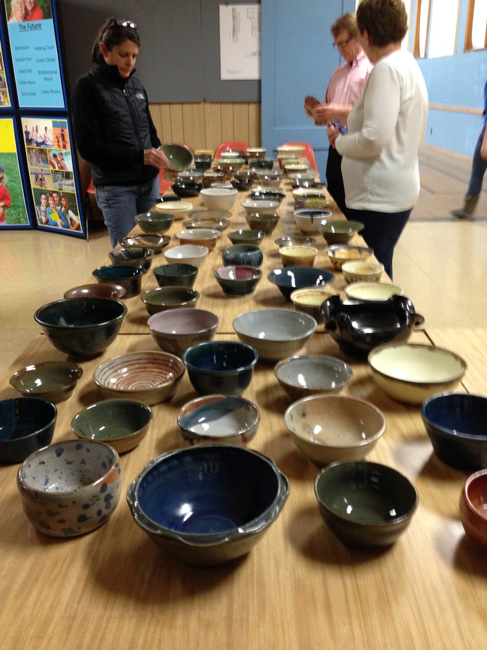 Photo of three people standing at a table with dozens of empty ceramic bowls