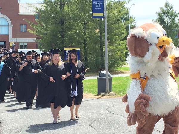 Photo of graduates outside marching behind owl mascot