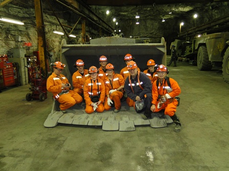 Nine people on a mining field trip posing with heavy equipment