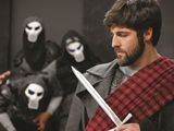 Photo of man holding a dagger with three people in masks behind him in the play "MacBeth"