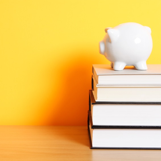 Photo of a stack of four books with a white piggy bank sitting on top of them