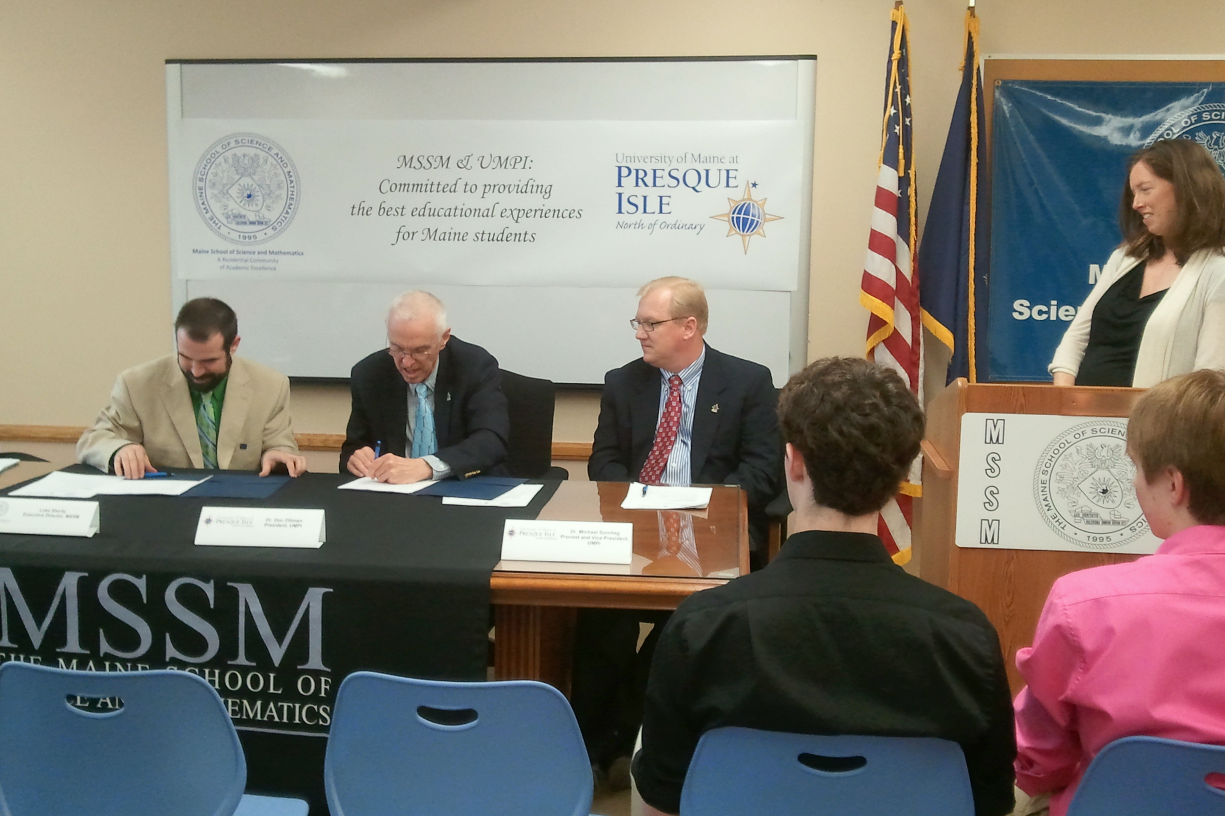 Three people signing the agreement with three onlookers