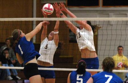 Photo of a volleyball player spiking the ball with two players on the other side of the net, attempting to block the spike